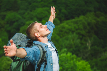 Freedom, discoveryand adventure concept. Young happy man with backpack standing on the edge of cliff.