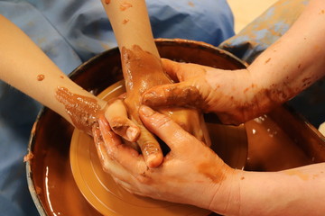 Close up of adult's and child's hands working together with clay on potter wheel 