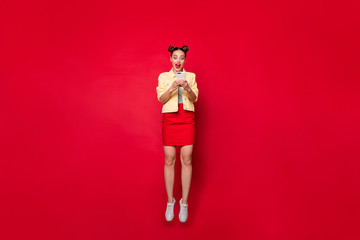 Full body photo of pretty jumping lady holding telephone hands wear casual outfit isolated red...