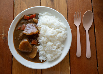 Top-view japanese curry rice or Kare Raisu in white dish on wooden table with folk and spoon