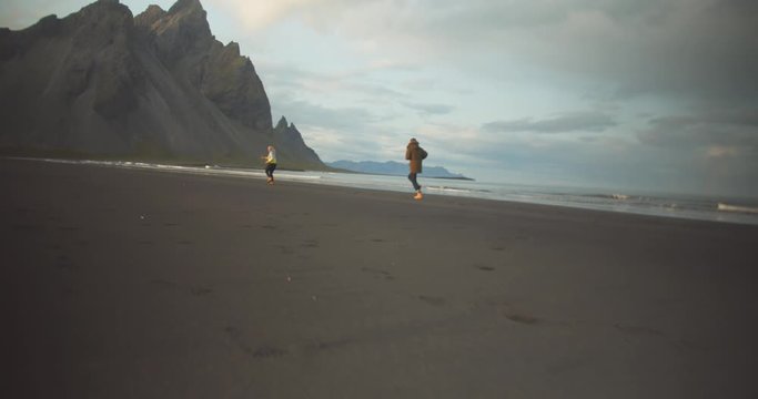 Couple running over black sandy beach with rocky hills in the background
