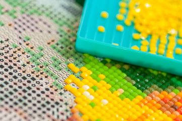 Collecting diamond embroidery, diamond mosaic. Colored crystals. Needlework. Creation. CloseUp.