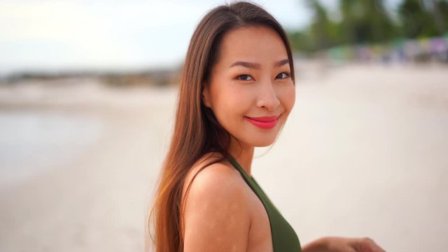 Static shot of a beautiful sexy Asian lady standing on the beach and smiling at the camera