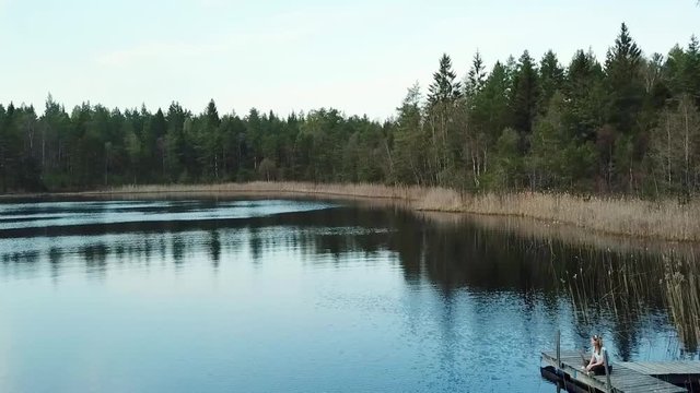 Person sitting on the edge of a lake in nature surrounded by forest