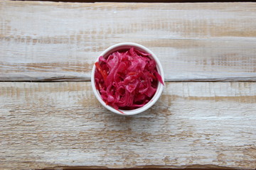 Red pickled cabbage in white bowl on wooden background