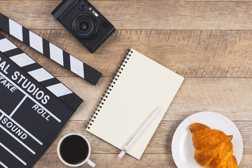 Movie clapper with paper, pen, cake and cup of coffee on wooden planks background