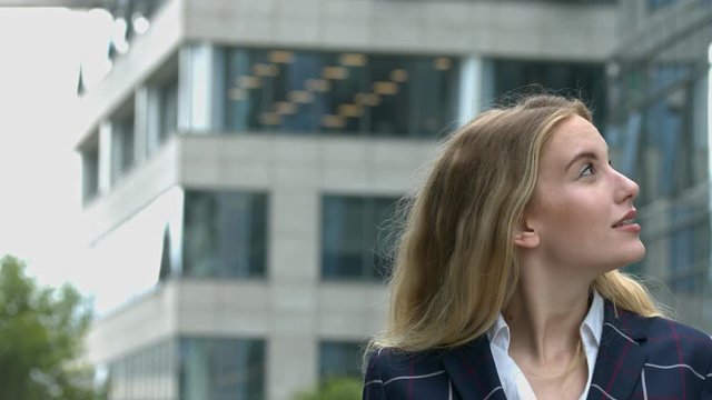 Beautiful young office worker looks up at city buildings skyscrapers slow motion closeup outdoors