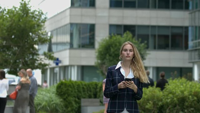 Beautiful young millennial businesswoman walks in city using phone slow motion