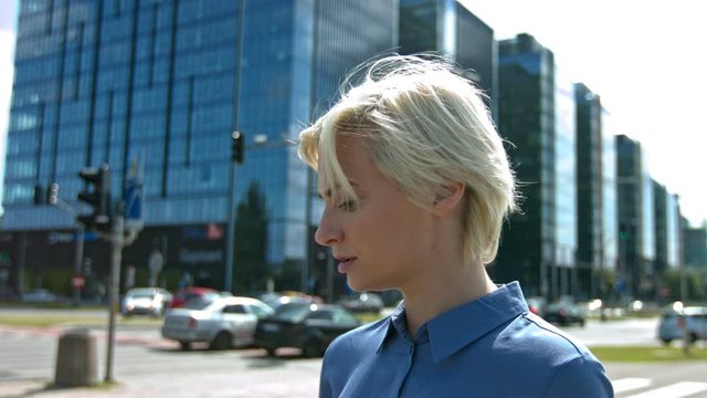 Blonde female professional standing in city looking around as cars pass by