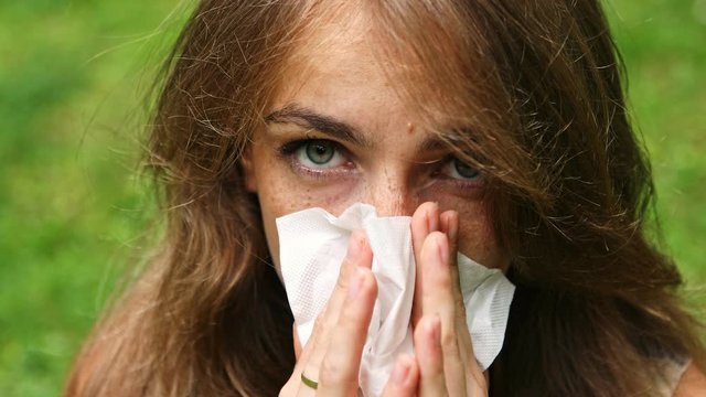 Sick girl with runny nose sneezing hard into tissue. Flu season concept.