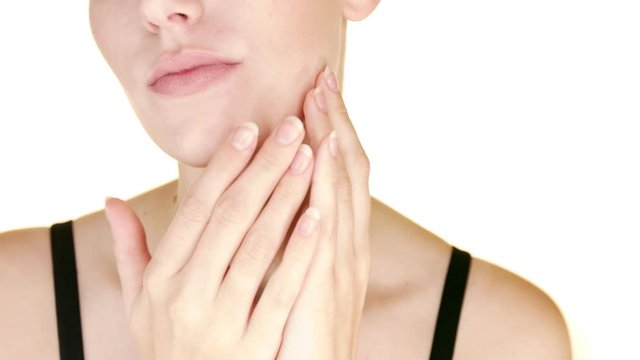 Close up of young woman's face gently massaging her cheekbones. White studio background.