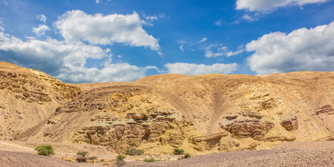 Middle East world heritage Judean desert nature scenery landscape view of sand stone wasteland foreground and rocky mountain background with blue sky white clouds 