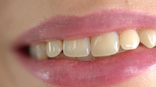 Close up shot of woman's teeth and lips. Wisp of hair slowly falling on her lip.