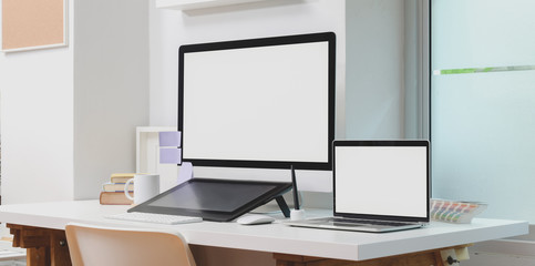 Blank screen desktop computer and laptop computer with office supplies in modern workplace