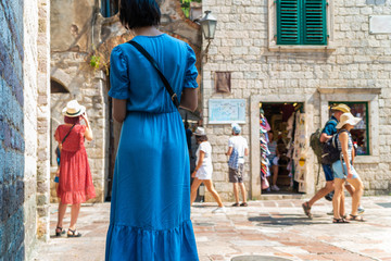 Tourists walking around downtown of Kotor. People on the background of the old stone city walls. Woman in a blue dress looking at passers-by. Travel and hobby lifestyle. Active vacations.