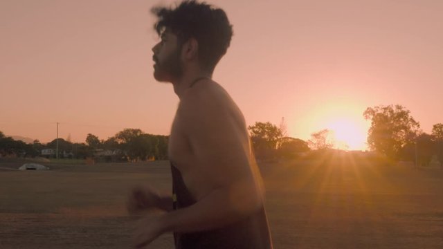 Indian guy running and trainning for cardio exercise on public park during sunset.