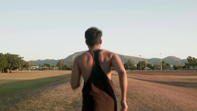 Indian guy running and trainning for cardio exercise on public park during sunset.