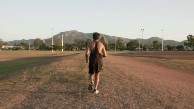 Indian guy running and trainning for cardio exercise on public park during sunset.