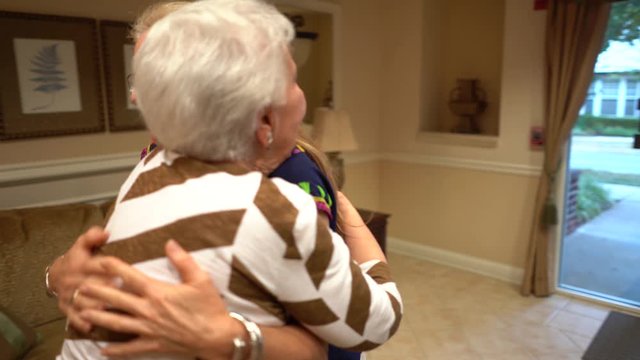 Camera orbits around blonde woman hugging elderly woman and rubbing backs.