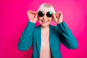 Close-up portrait of her she nice attractive cheerful cheery funky gray-haired lady wearing blue green jacket touching cool specs isolated on bright vivid shine vibrant pink fuchsia color background