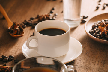 A cup of coffee with water, coffee beans and tea on wooden bakcground