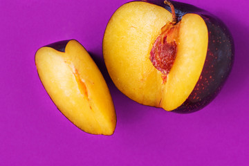 Big ripe organic purple plum with cut out segment on vibrant violet background. Creative trendy minimalist food poster banner with copy space