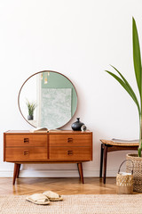 Minimalistic and stylish composition of living room with wooden commode, mirror, tropical plant, footrest and elegant personal accessories. Interior design, Home decor. template. White walls.