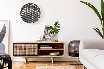 Stylish scandinavian living room interior with gray sofa, black lamp, design commode, tropical...