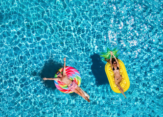 Glückliches Paar auf bunten Luftmatratzen treibt über blaues Pool Wasser