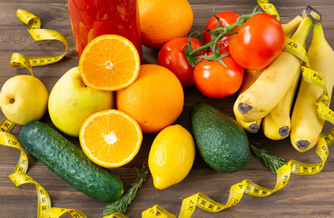 oranges, lemon, apples, bananas, tomatoes, avocado, cucumbers, rosemary, a bottle of tomato juice on a brown wooden background, centimeter tape