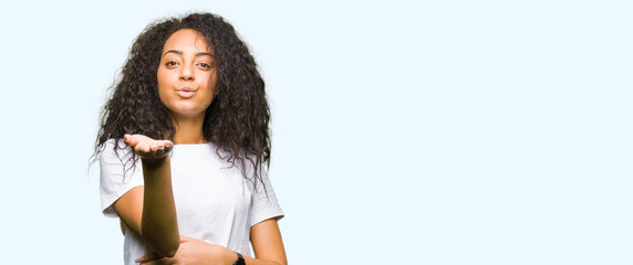 Young beautiful girl with curly hair wearing casual white t-shirt looking at the camera blowing a kiss with hand on air being lovely and sexy. Love expression.