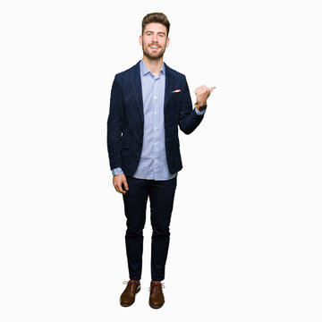 Young handsome bussines man smiling with happy face looking and pointing to the side with thumb up.