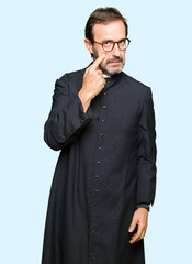 Middle age priest man wearing catholic robe Pointing to the eye watching you gesture, suspicious...