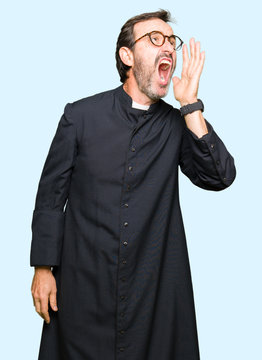 Middle age priest man wearing catholic robe shouting and screaming loud to side with hand on mouth. Communication concept.