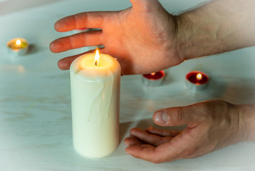 Hands drawn out above the burning candle. Burning candle symbol of eternity and remembrance of the dead. Home interior decor.