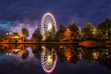Germany, Colorful illuminated ferris wheel and lights of giant swabian fair called cannstatter wasen in stuttgart city by night reflecting in neckar river water