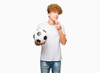 Young handsome man holding soccer football ball serious face thinking about question, very confused idea