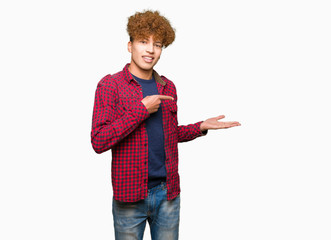 Young handsome student man with afro hair wearing a jacket amazed and smiling to the camera while presenting with hand and pointing with finger.