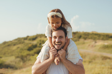 Father and daughet spending time together taking a walk in the green mountain fields on their vacation. Father holding the girl on his back.