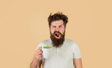 Yawning man with sleepy face try to awake with cup of coffee. Man hold mug with hot drink. Man with...