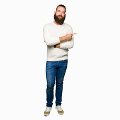 Fototapeta premium Young hipster man wearing winter sweater Pointing with hand finger to the side showing advertisement, serious and calm face