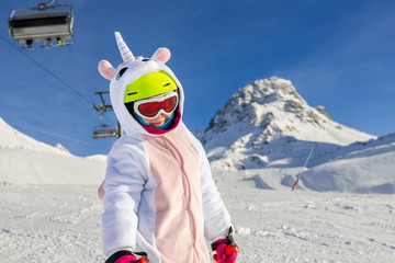 Cute adorable preschooler caucasian kid girl portrait with ski in helmet, goggles and unicorn fun...