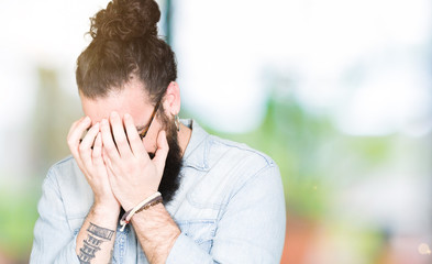 Young hipster man with long hair and beard wearing glasses with sad expression covering face with hands while crying. Depression concept.