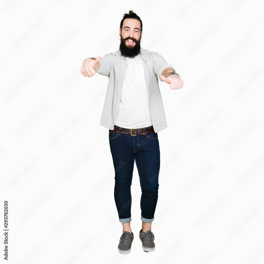 Wall mural young man with long hair, beard and earrings approving doing positive gesture with hand, thumbs up s