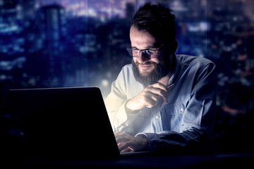 Young handsome businessman working late at night in the office with blue lights in the background