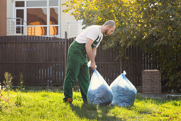Gardener picks up bags of leaves to remove debris from the territory. Green uniform