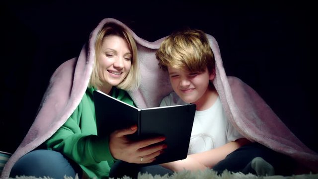 4K Dolly Shot of Mum and Son Reading Book under the Blanket