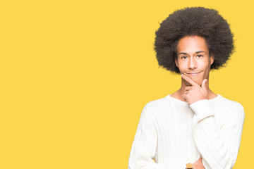 Fototapeta na wymiar Young african american man with afro hair wearing winter sweater looking confident at the camera with smile with crossed arms and hand raised on chin. Thinking positive.