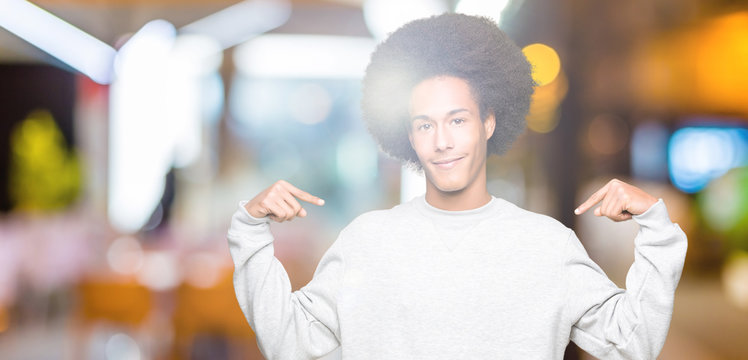 Young african american man with afro hair wearing sporty sweatshirt clueless and confused expression with arms and hands raised. Doubt concept.
