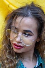Portrait of beautiful young woman with glasses and disheveled hair. With urban fashion on yellow cloth background.
